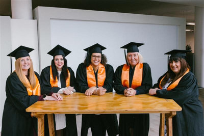 Group of B&Q employees in graduation caps and gowns around a table at B&Q's Store Support Office.