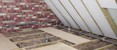 Loft space with pipes running along joists and wall covered in foam pipe insualation.