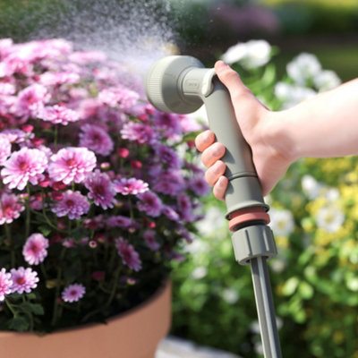Person watering plants in a plant pot with a hose.