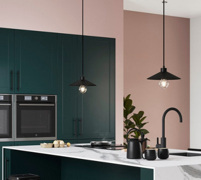 Two statement black pendant lights hanging above a kitchen island in a dark green and pink kitchen.