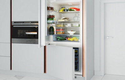 A close up view of a white gloss kitchen integrated cabinets of fridge and freezer, with rose gold background.