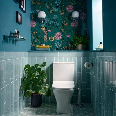 A charming blue bathroom with blue wall tiles, a white toilet, and a teal bird and flower wallpaper feature wall.