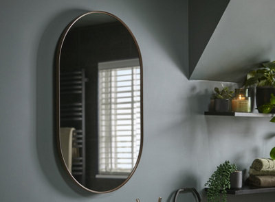 An oval bathroom mirror installed on a dark green wall.