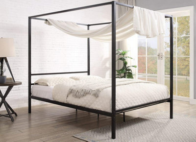 A black metal four-poster bed in a bright and airy bedroom space.