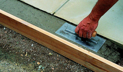 Using a concrete float to level concrete that has been laid between a timber support and paving slabs.