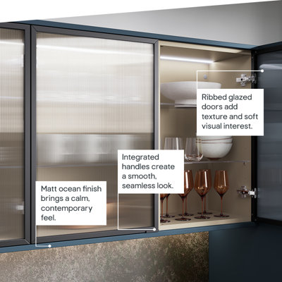 The Garcinia kitchen features matt slab doors with integrated handles in a deep tone, complemented by ribbed glazed wall units for a calm, contemporary look.
