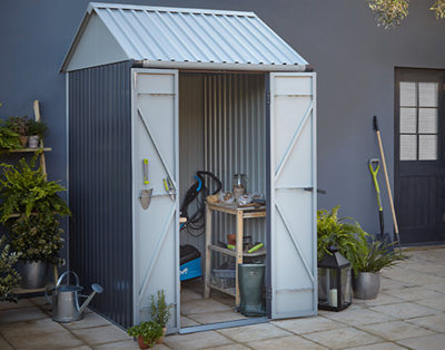 A small metal shed with an apex roof installed on a patio, with gardening equipment stored inside.