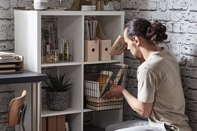 Items are being organised in a basket within one section of a white cube shelving unit.