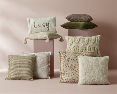 A collection of decorative pillows in soft, neutral tones arranged against a beige background.