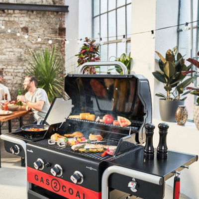 Large hybrid barbecue with food cooking on the grill in a garden.