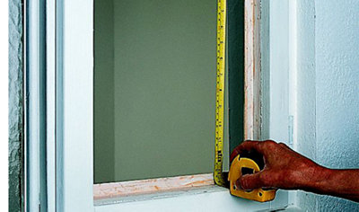 Person using a tape measure to calculate the size of glass needed for a casement window.