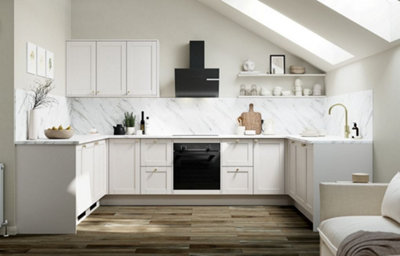 Bright dove grey shaker kitchen with marble-effect splashback and worktops, integrated oven, black cooker hood, brass tap and handles, open shelving, and sloped ceiling with skylights.