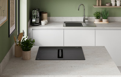 The Garcinia kitchen in gloss dove grey, featuring smooth slab cabinet doors with integrated handles, a stone-effect worktop, and a green painted splashback for a calm, contemporary look.