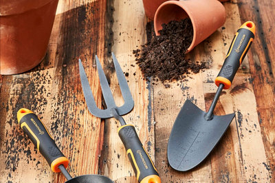 A garden hand trowel and hand fork on a wooden table with plant pots and compost.