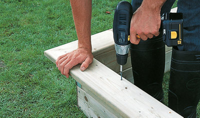 Person using a drill and decking screws to secure a sandpit seat to a sandpit frame.