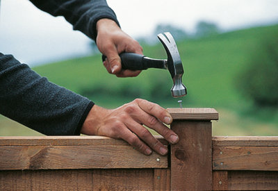 Person using a hammer and nail to secure a timber fence post cap to the top of a fence post.