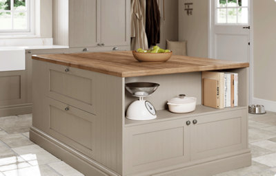 A kitchen island is finished in a shaker style in matt warm grey. There is a combination of drawers and open shelving around the island. The countertop is a warm shade of wood.