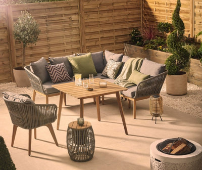 A grey garden sofa with green cushions and blankets, a grey arm chair, and wooden table in a paved garden.