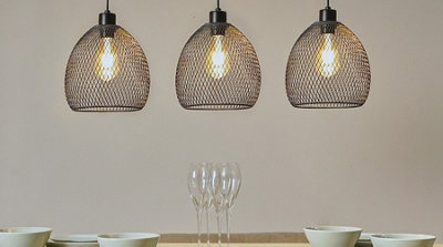 Three black mesh wire domed pendant lights hanging low above a dining table, creating a bold, industrial look.