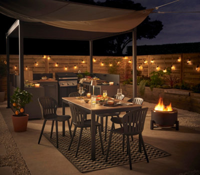 Large garden at night time with dining table and outdoor kitchen surrounded by twinkling fairy lights.