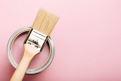 A can of pink paint with a light brush on it against a pink background.