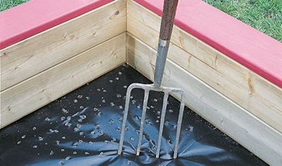 Using a garden fork to create drainage holes in a pond liner at the bottom of a sandpit.