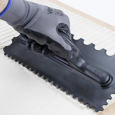 Gloved hand using a tiling tool to smooth grout