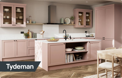 The Tydeman kitchen, featuring shaker style cabinets in a soft pink shade, paired with black handles. Both the L-shaped kitchen and the kitchen island have a white countertop.