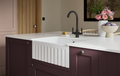 The Tydeman kitchen, featuring shaker style cabinets in a deep rich purple colour, with silver coloured handles. The kitchen features a mix of white marble-effect countertops on the kitchen island.