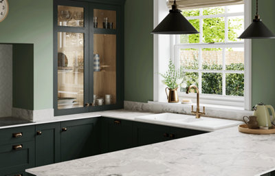 The Tydeman kitchen, featuring shaker style cabinets in a dark shade of green. Cabinets are paired with brass hardware, and marble-effect countertops feature on the kitchen worktop, splashback, and envelope the kitchen island.