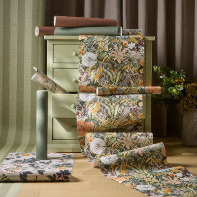 Styled interior featuring botanical print wallpaper draped over a sage green chest of drawers, with coordinating striped wallpaper backdrop and decor accessories on a wooden floor.