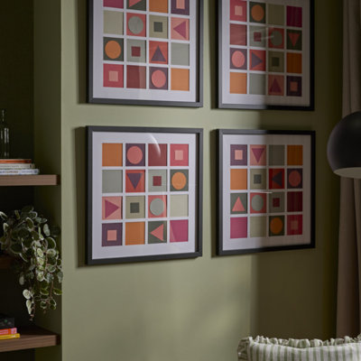Gallery wall of framed geometric prints arranged in a grid on a green wall, featuring warm-toned shapes in orange, pink and red.