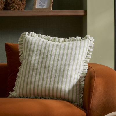 Green and white striped cushion with ruffled edges styled on an orange armchair, showing soft fabric and relaxed folds.