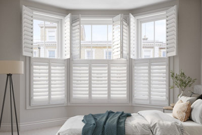 White shutters installed on a bay window in a cream painted bedroom.