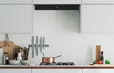 A gas hob mounted on a light coloured worktop, with various utensils and white herringbone patterned tiles on the wall.