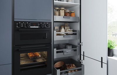 A close up of a black built-in oven surrounded by matt blue cabinets and wooden worktops.