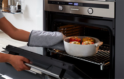 A person is using oven mitts to remove stuffed peppers from an oven.