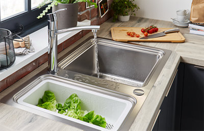 Water runs from a tap into a stainless steel dual-sink. In the smaller half of the sink, lettuce is draining.