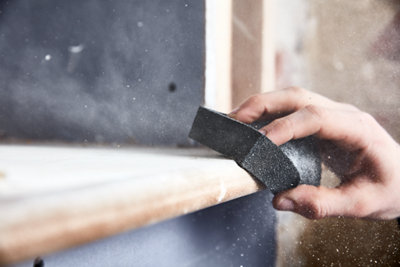 A person is using a sanding block to sand down a piece of wood.