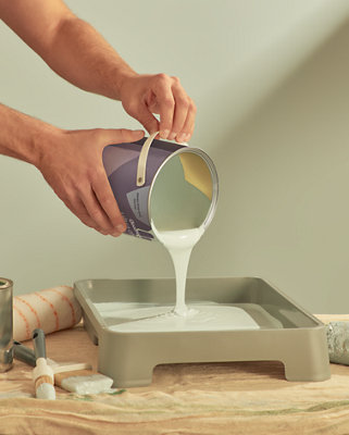 Pouring paint from a pot into a paint tray.