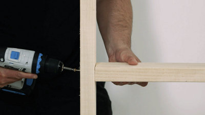 Person using a drill to drive a woodscrew through a vertical stud to secure a horizontal nogging on the other side that they are holding in place.