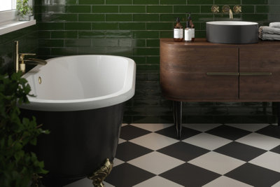 Black and white checkerboard tiles in a dark green bathroom with a black roll top bath and dark wooden vanity unit with freestanding grey basin.