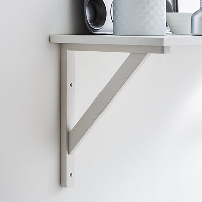 White wood triangle shaped shelf bracket mounted on a white wall supporting a white shelf.