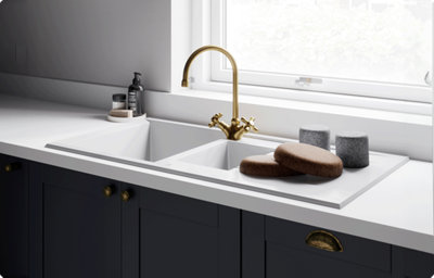 A matt white sink sits within a white kitchen countertop. The tap is a brushed brass colour.