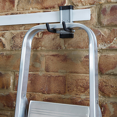 Close up of step ladder hanging from metal ladder hook with two small metal arms.