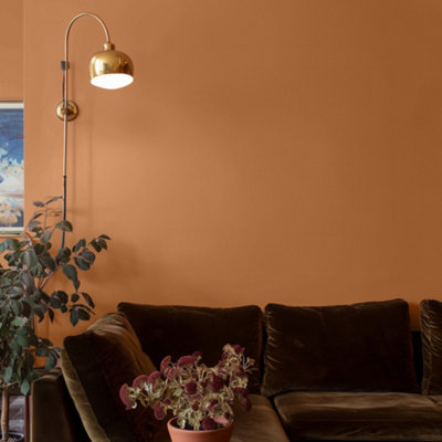 A warm terracotta living room painted in Lick's orange 02 with a brown sofa and gold lamp.