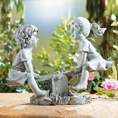 Adorable boy & girl see-saw statue with hand-painted details. Polyresin with a weathered stone look. H28 x W33 x D13.5cm