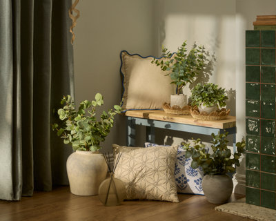 Cosy corner with potted plants, textured cushions, and a wooden bench. Natural light casts soft shadows, creating a serene and inviting atmosphere.