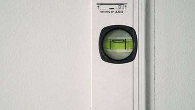 Spirit level laid flat on a wall with the bubble in the centre indicating it's level. Pencil line has been drawn next to the spirit level.