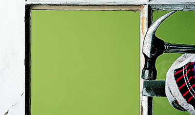 Person using a hammer to strike a chisel, carefully removing old putty from the edge of a window frame.